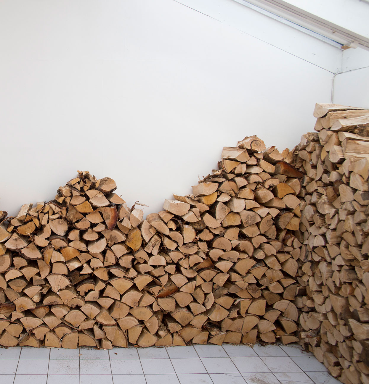 piles of wood in a corner of a white room.