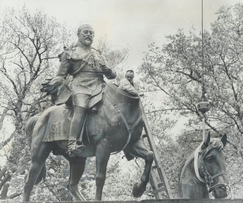 Grey photograph of statue of man on headless horse. Man on ladder preparing to install horse head. 